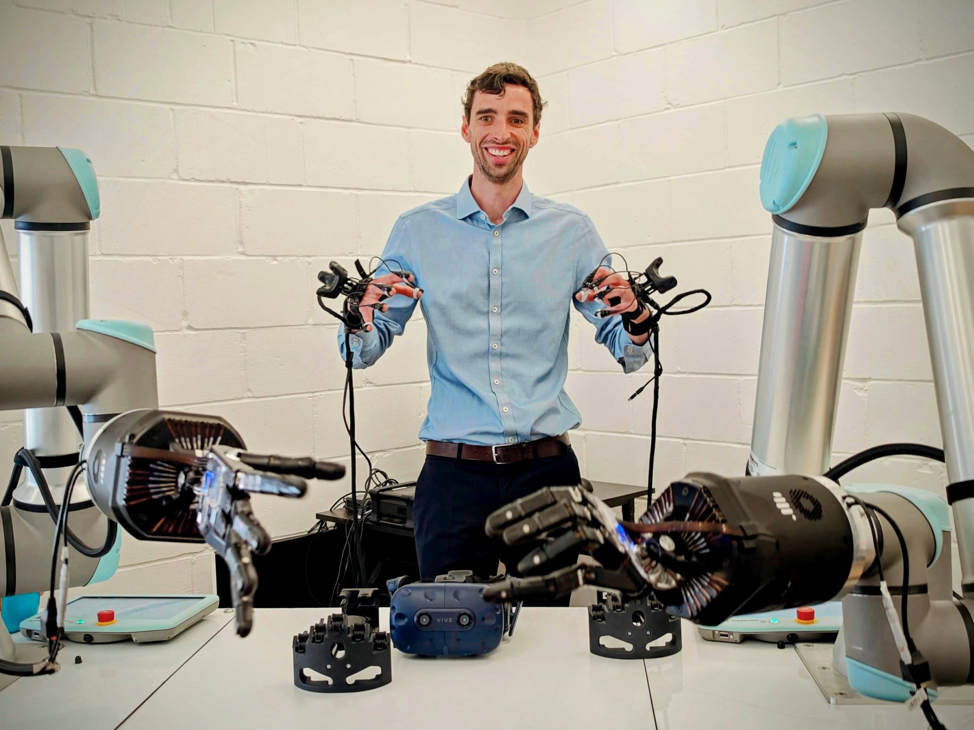 Olivier wearing motion-tracking gloves, controlling two robot hands on robot arms
